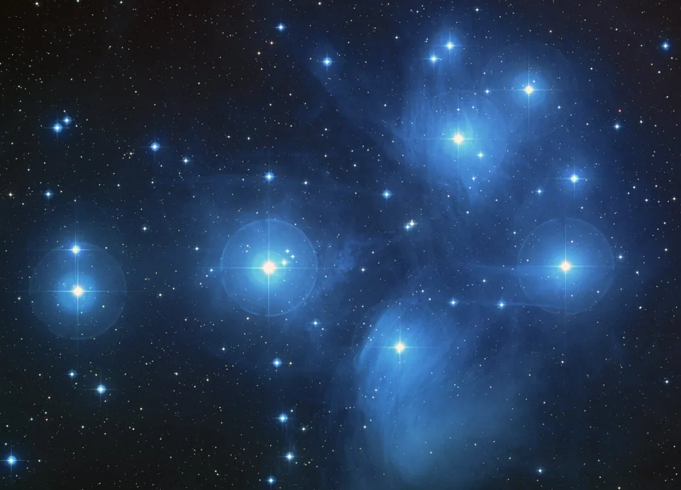 Blue reflection nebulae around the bright stars of the Pleiades cluster.