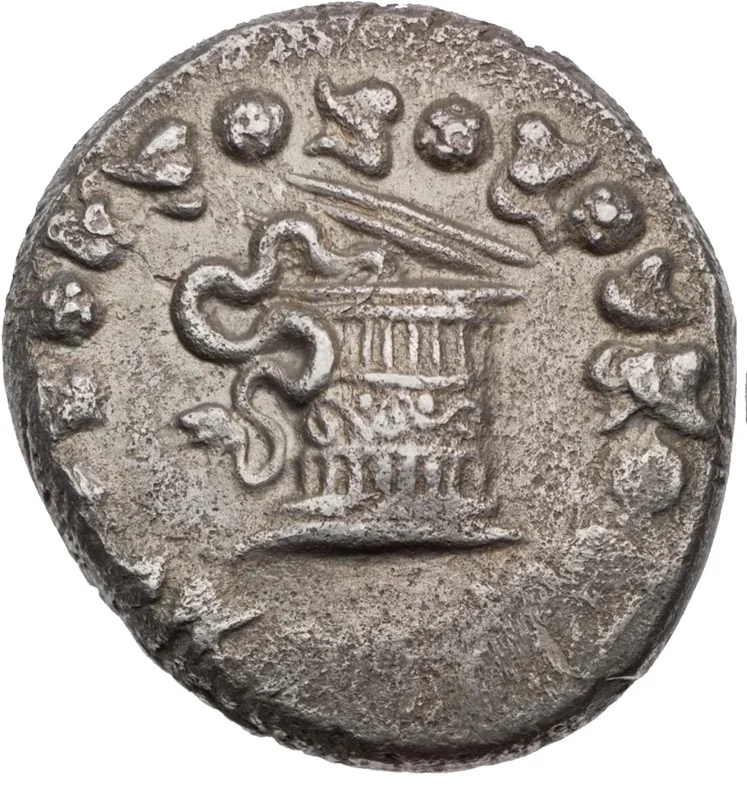 A worn silver coin showing a round lidded wicker basket inside an ivy wreath, its lid pushed half open and a serpent winding out of it to the left.