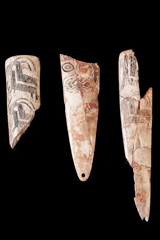 Three pale carved bone plaques on a black ground, the middle one pointed and pierced at its narrow end.