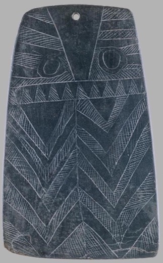 Engraved slate plaque with two large owl-like eyes above chevron bands, a single hole drilled at the top centre.
