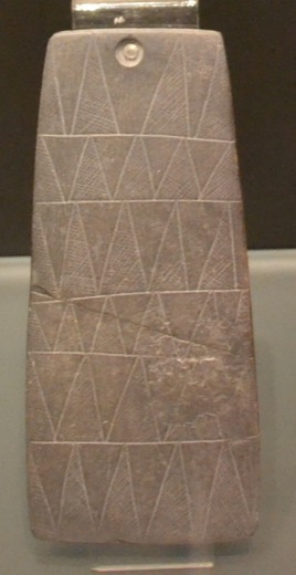 Tall trapezoidal slate plaque engraved with rows of hatched triangles, single perforation at the top.