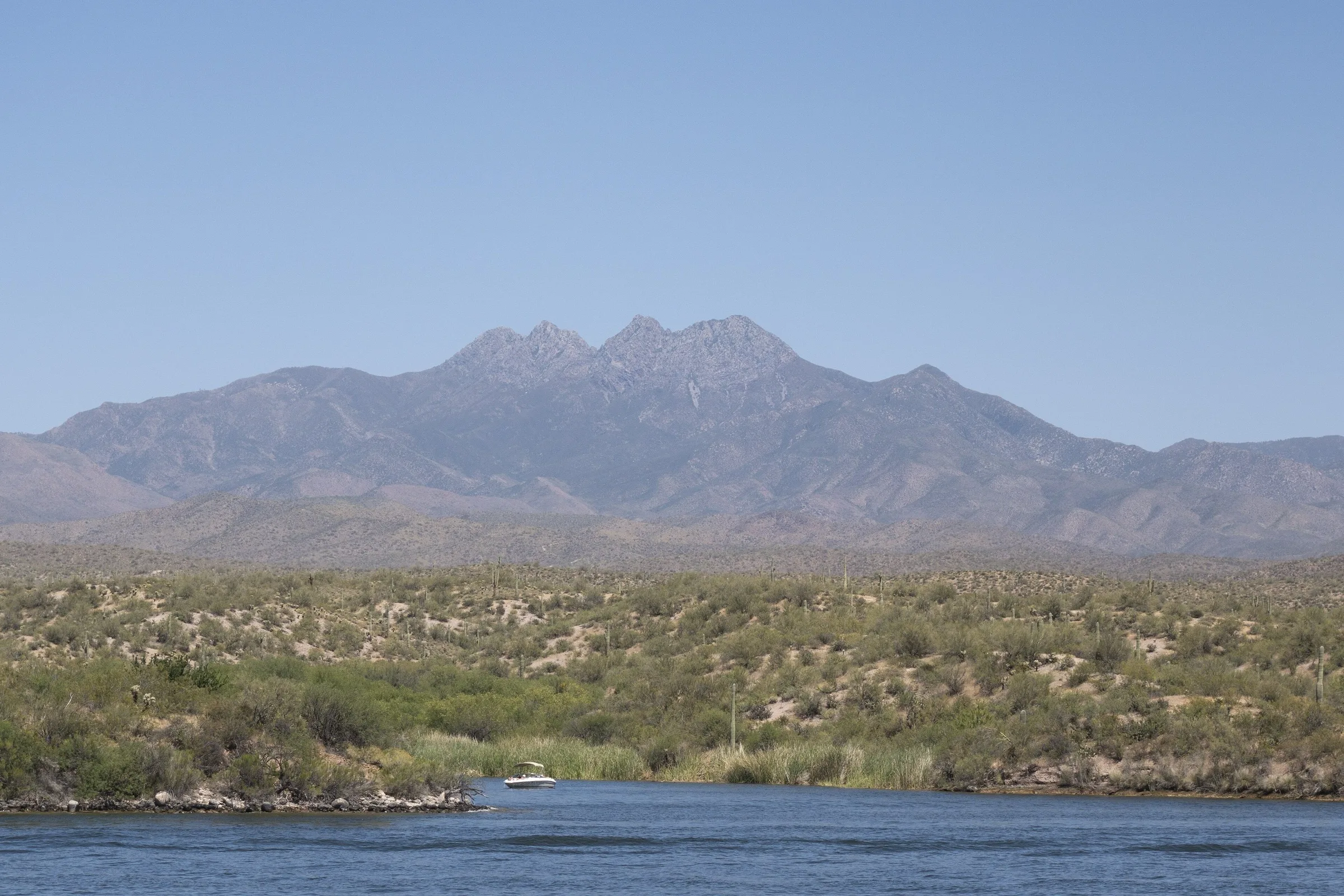 The four granite summits of Four Peaks rising above saguaro desert, with a blue river channel in the foreground.
