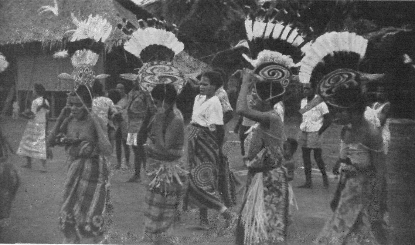 Men at the Bonggrang feast in tall headdresses: carved half-circle boards painted with spirals, crowned with white feathers and birds of paradise.