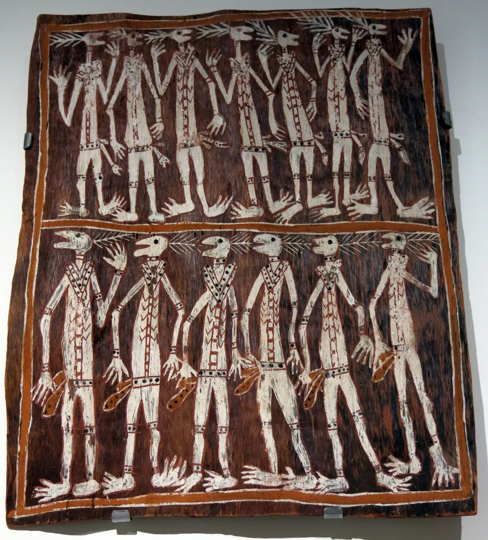 A bark painting of two rows of Kunapipi dancers, their long white limbs and radiating head adornments standing out against red-brown bark.