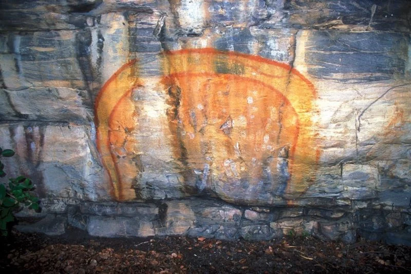 A broad red and yellow serpent figure painted across the uneven rock wall at Ubirr, Kakadu.