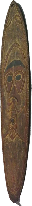 A worn, elongated wooden board carved with a frontal figure: large round eyes, a broad nose and mouth above a smaller body motif.