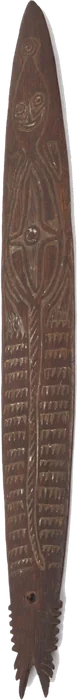 A slender dark bullroarer incised with a long figure, its lower end cut into a forked tail.