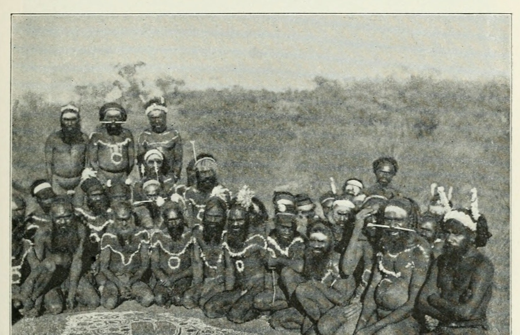 Decorated men of the Emu totem sitting around a churinga design drawn on the ground