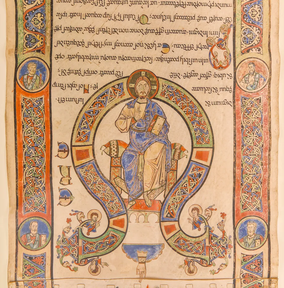 A section of an illuminated parchment roll: Latin text written upside down above a painting of Christ enthroned within a great interlaced initial, with bordered columns of saints in roundels on either side.