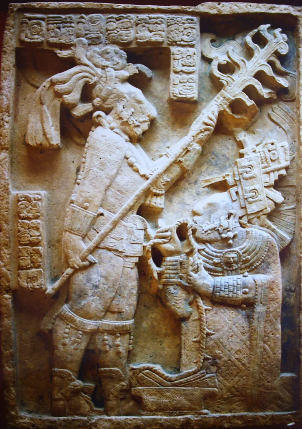 A carved lintel: a standing king holds a flaming torch over a kneeling woman, who draws a thorned rope through her tongue into a basket.