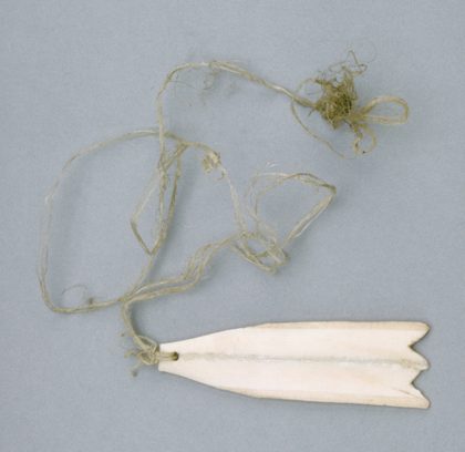 The Belcher Islands blade itself — pale bone, forked tail, its plant-fibre cord through the one hole.