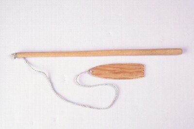 Yup’ik levlugtaq from Toksook Bay: a long pale wooden handle above a shorter flat wooden blade, joined by a looped cord.