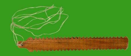 A serrated wooden slat pierced near one end for its cord — the bull roarer donated to the museum by Donnchadh Ó Floinn of Maynooth, Co. Kildare.