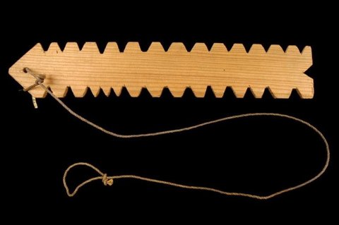 A long pale wooden bullroarer blade with many small notches cut along its edges, shown with its cord.