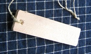 A pale rectangular Bulgarian bramkalo blade with a cord through a hole near one end, photographed on blue plaid cloth.