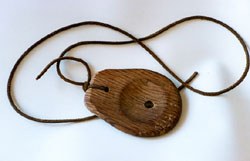 The zumbador itself: a small oval piece of encina (holm oak) wood on a leather cord, from León.