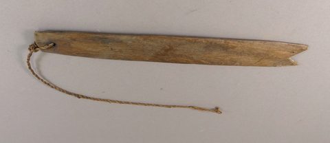 A weathered wooden bull-roarer with a forked swallow-tail notch at one end and a twisted cord at the other.