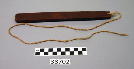 A plain rectangular wooden board with a cord tied through a hole at one end: a Hopi To-Wok-Kin-Pi from Oraibi, shown for the general North...