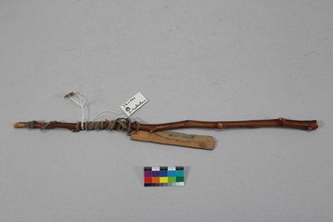 A flat Schwirrholz blade bound by its cotton cord to a twig handle, collected at Kara Khoja by the Second Turfan Expedition, 1904–1905 — the...