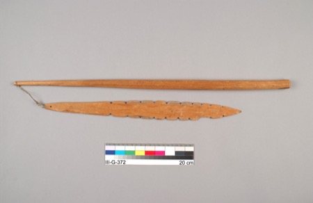 An Anishinaabe bull-roarer from Lac Seul, Ontario: a scallop-edged wooden blade on a cord tied to a slender handle, meant to be swung overhead...