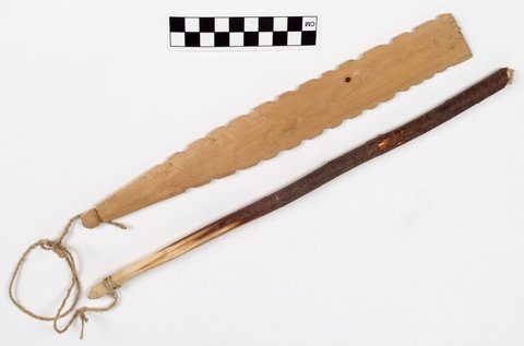 Swampy Cree bullroarer from Cross Lake, Manitoba: a pale wooden blade with teeth along both edges, joined by cord to a long handle.