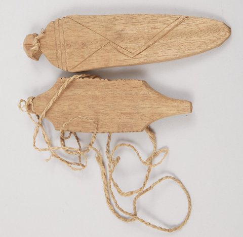 Two wooden bullroarers from the Pagai Islands: the upper broad blade has crossed V-shaped incisions, while the narrower lower blade has toothed edges; cords trail from both.