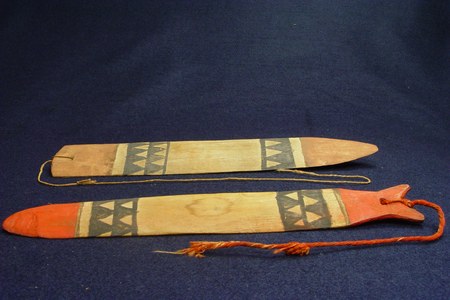 Two Kuikuro zunidores from the Upper Xingu, laid out on blue cloth: painted wooden slats banded with dark triangle motifs, one tipped in red...