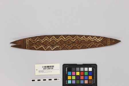 The documented Kubka/Kubkin bullroarer: a painted, relief-carved wooden slat about 40 cm long, its zigzag and dotted bands set inside a diamond...
