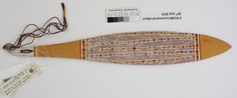 Painted Gupapuyngu Daygurrgurr burala from Howard Island: a long ochre blade with a pointed end, white diagonal bands and dotted borders, with cord attached at the pierced end.