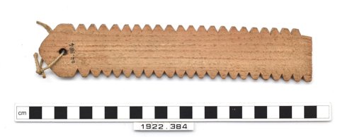 Ickleton wooden buzzer with serrations along both long edges and a cord through a hole near one end, shown above a scale.