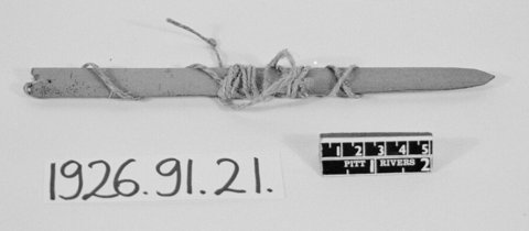 Yoruba palm-midrib bullroarer from Oyo: a single long narrow blade with a squared end and pointed opposite tip, its cord wound around the middle.