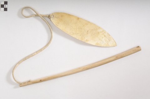 Pale rawhide bullroarer blade linked by a long flat cord to a slender wooden handle; made by Norman Joseph Plante in Belcourt, 1968.