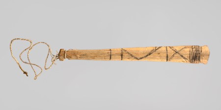 A pale wooden slat painted with bold black zigzags and a cross-hatched band toward its squared tip, twisted cord tied at the knobbed grip — a...