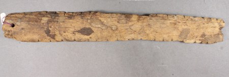 A weathered, saw-toothed wooden bull-roarer excavated at site CA-LAn-295 in West Hills, Los Angeles County — shown for the southern-California...