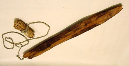 A long, dark wooden blade tapering to a point, with a coil of cordage lashed at the broad end — a Pomo bull-roarer collected at Coyote Valley...