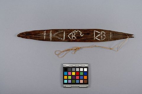 A companion sova from the Sirorata gift, with pale geometric figures and bands along its dark wooden blade, still on its bark-fibre cord.