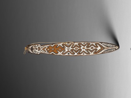 A dark wooden blade carved at its flared, corded handle end with a stylised face, the rest of the surface covered edge to edge in white,...