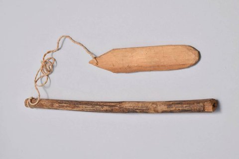 A wooden rod handle tied by a cotton cord to a flat oval wooden blade.