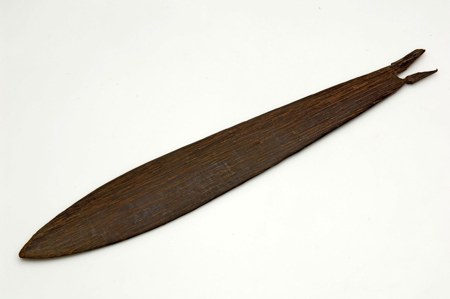 A plain dark wooden bullroarer, its strongly grained blade tapering to a point at one end and a small forked tip at the other - a ceremonial...