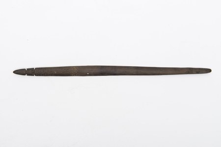 A Bogadjim bull-roarer collected by Kapitän Rohde in the nineteenth century — a long, slender dark blade, its spear-point tip cut nearly free...