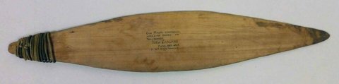 A Māori pūrerehua in the Pitt Rivers Museum, Oxford, with a broad pale wooden blade and cord wrapped around its narrow end.