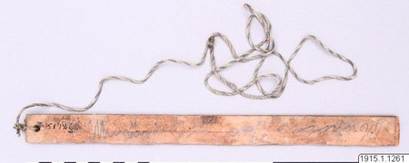 Itonama bull-roarer, Bolivia — a pale wooden slat inscribed in pencil with collection notes, its plaited cord looped loosely at the perforated...