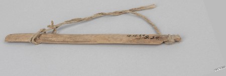 Guarayu bull-roarer, Bolivia — a slender pale lath, its cord wrapped and knotted around both ends so it hangs in a long loop, collected by...