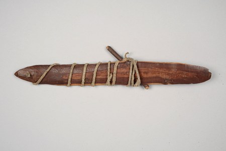 A San Schwirrholz photographed with its cord and winding stick: an oval blade carved with a central leaf-like spine and a drilled hole near the...