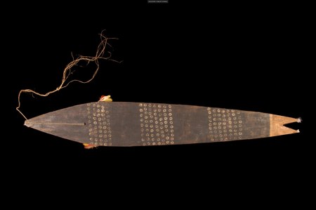 The Bororo aige itself: a dark blade stippled with bands of small dotted circles, red-and-yellow feather tufts at its edges, corded through a...