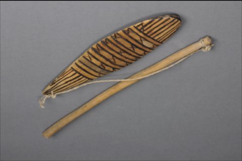 A Kereboro bull-roarer rig with a leaf-shaped blade painted in dark bands, a separate long stick, and a connecting cord.