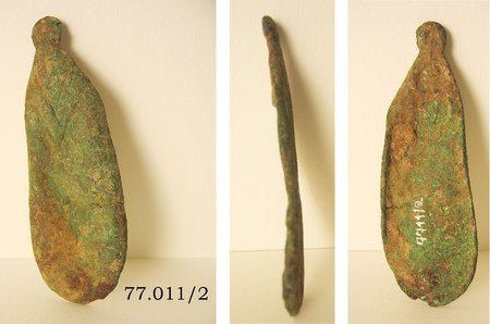 The Djenné bromhout in three museum views: a corroded green copper-alloy blade, leaf-shaped with a rounded lower end, rising to a small solid...