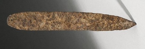 A Tusia iron rhombe from Burkina Faso, a thin rusted metal slat with one rounded end and one tapered point.