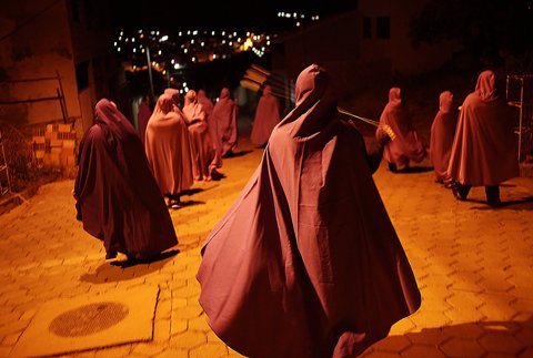Itapecerica’s 2016 soul-prayer procession, with hooded people walking along a warmly lit street at night.