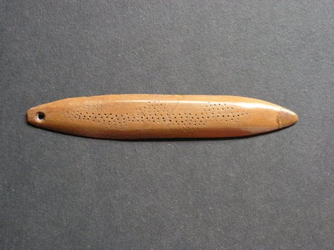 The Havelland bullroarer itself: a slender, biconical bone blade polished to a soft sheen, with faint fields of drilled dots patterning both...